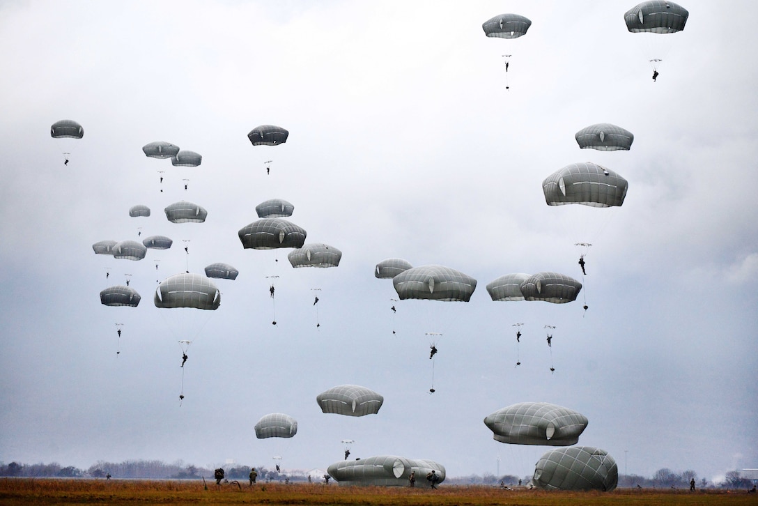 Soldiers drift to the ground using parachutes.