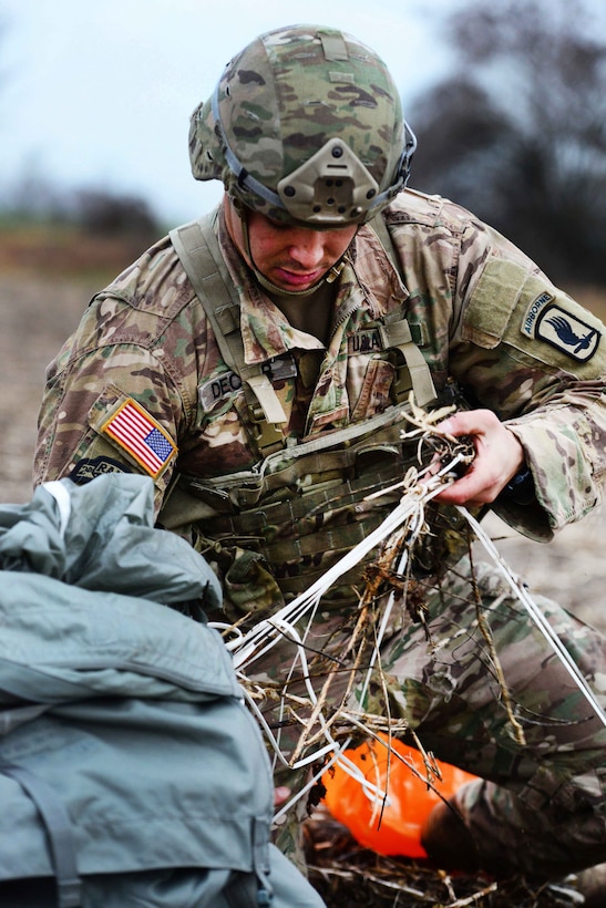 A soldier picks up a parachute from the ground.