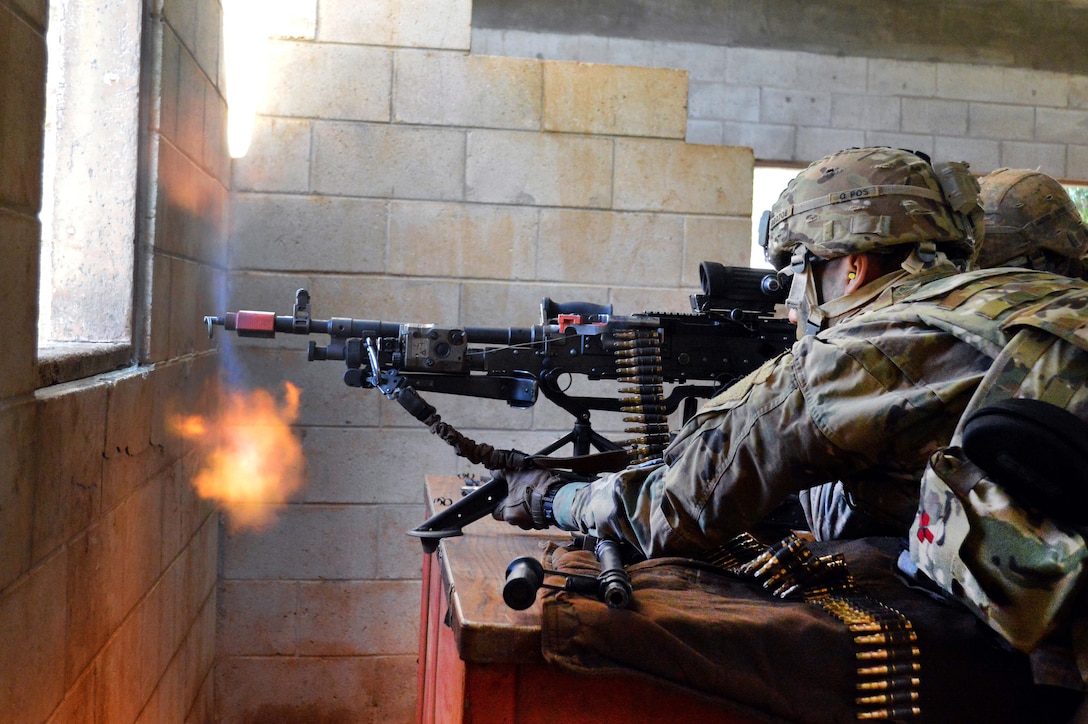 Soldiers fire a machine gun out the window of a building.