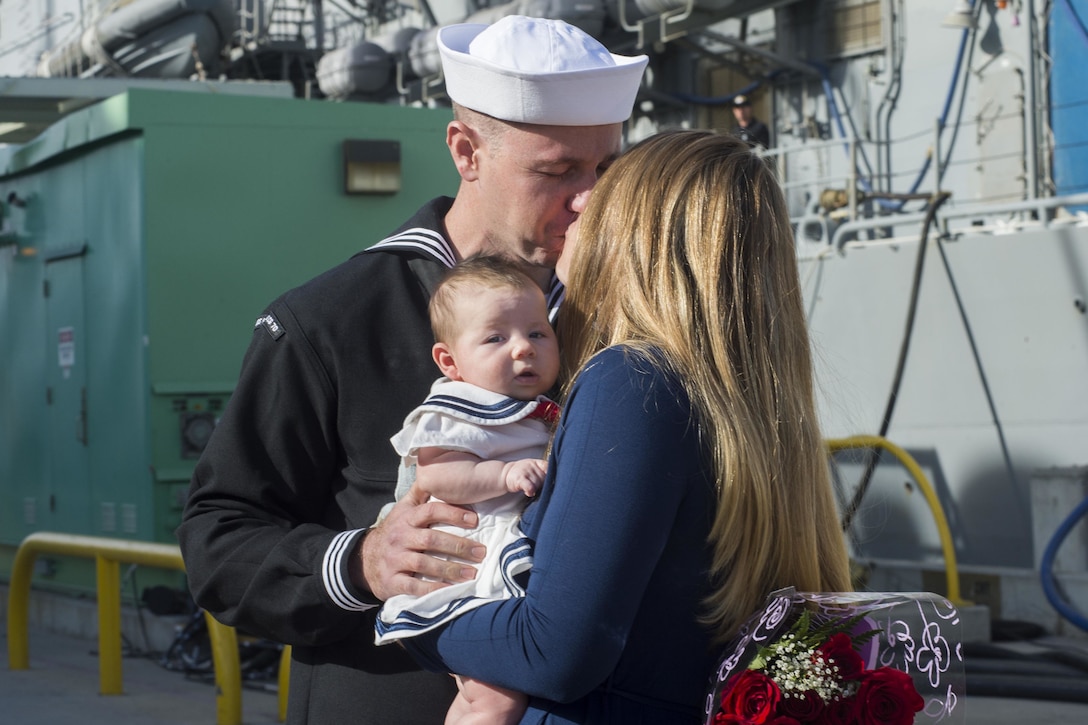 A sailor kisses a women holding a baby.