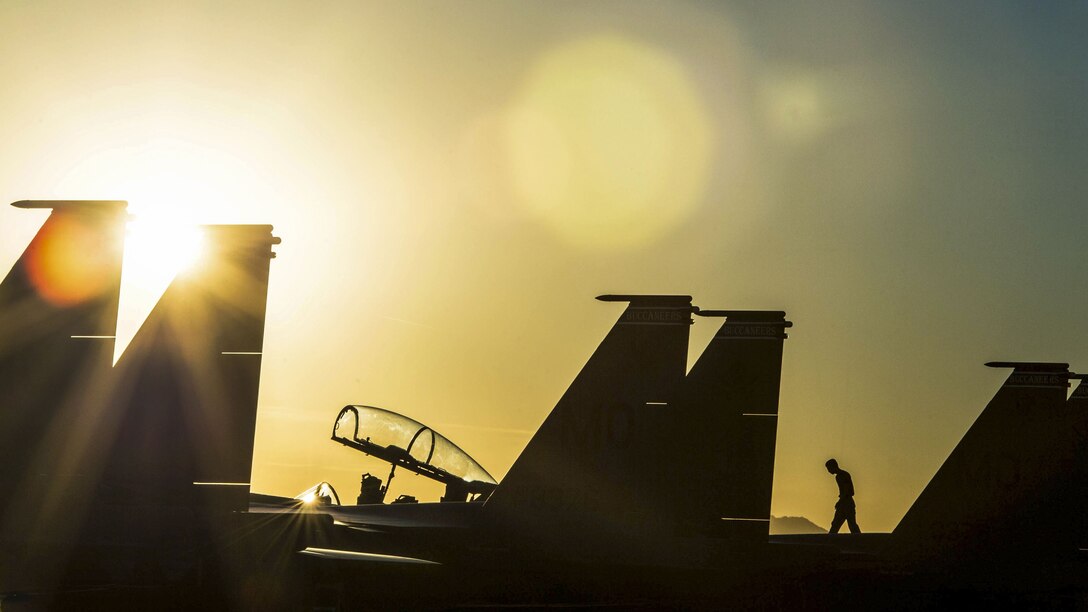 A service member, shown in silhouette, walks atop a parked aircraft on a flightline.