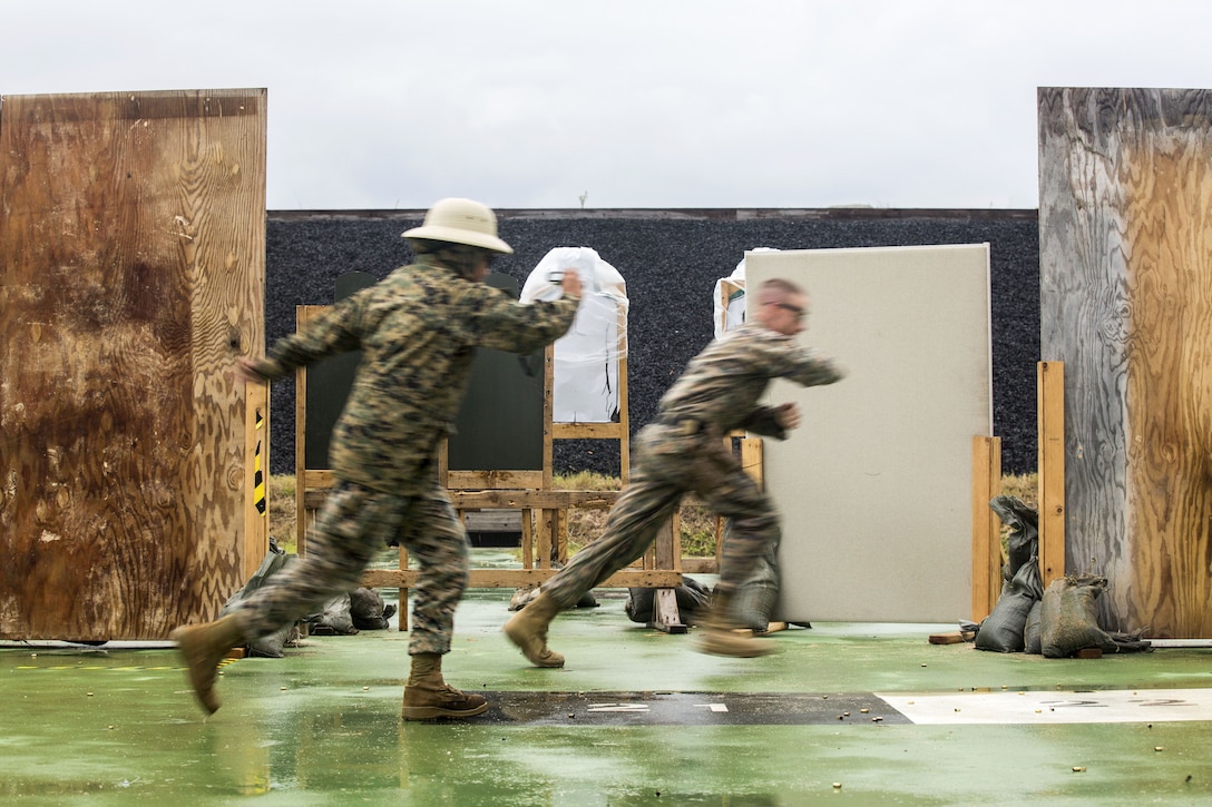 Two Marines run in a room between wood structures.