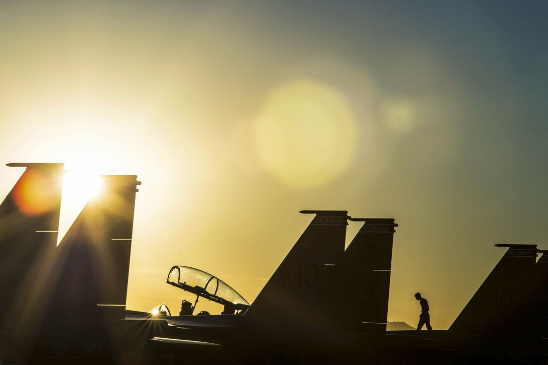 A service member, shown in silhouette, walks atop a parked aircraft on a flightline.