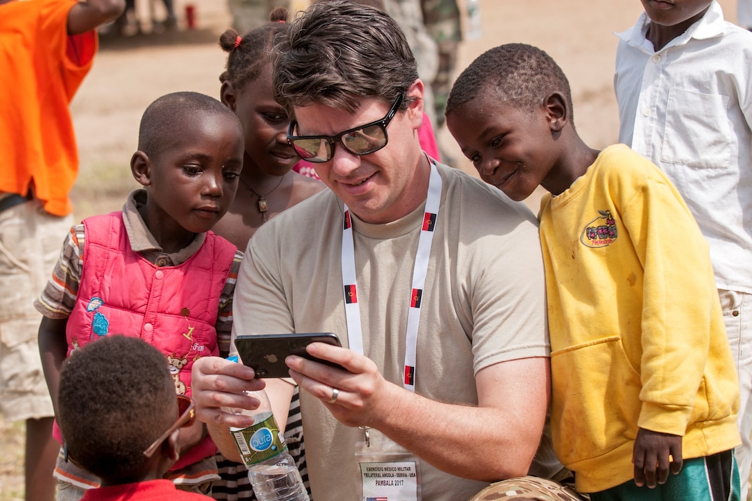 Maj. Chase Scarborough, an Ohio Army National Guard dermatologist participating in the PAMBALA medical exercise, entertains children outside one of the field hospital clinics in the village of Vale do Paraiso during phase 2 of the exercise Dec. 11, 2017, in Bengo Province, Angola. PAMBALA is the first-ever trilateral combined medical engagement to take place in the Republic of Angola, highlighted by a four-day clinical operations mission focusing on services like preventative medicine, pediatrics, family practice, dermatology, optometry, dentistry, and obstetrics and gynecology at various field hospitals in the province. The historic engagement aims to build the foundation for future engagements between the U.S. and Angola, as well as enhance the 11-year partnership the Ohio National Guard maintains with Serbia, through the National Guard State Partnership Program. (Ohio National Guard photo by Staff Sgt. Wendy Kuhn)