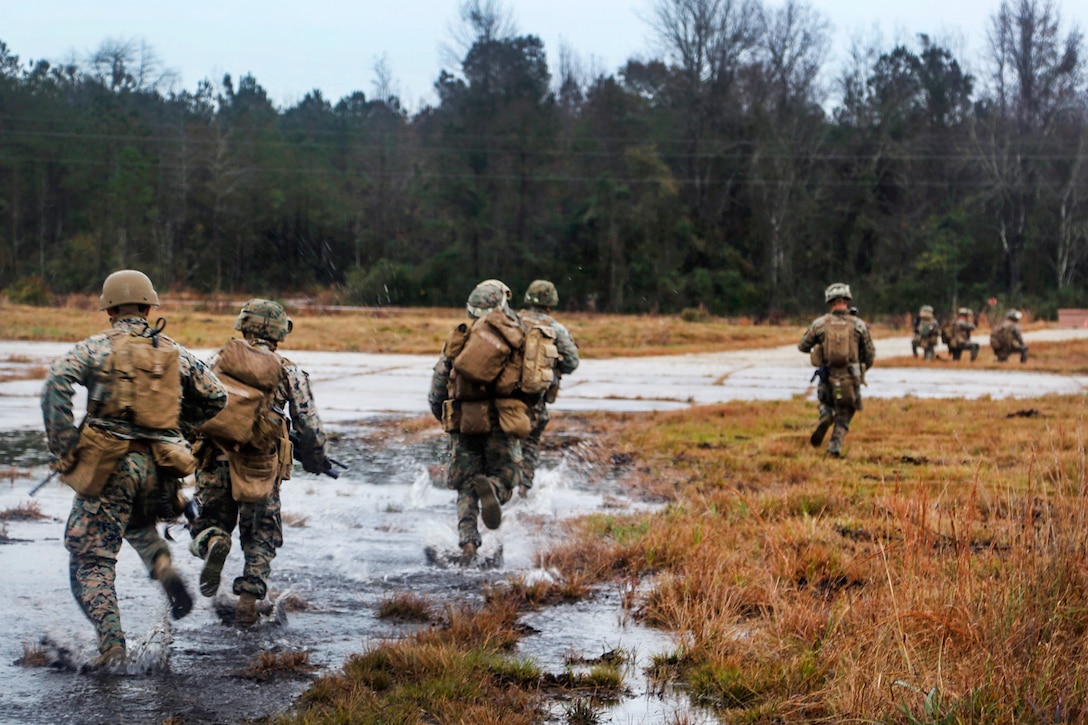 Marines run though marsh and water.