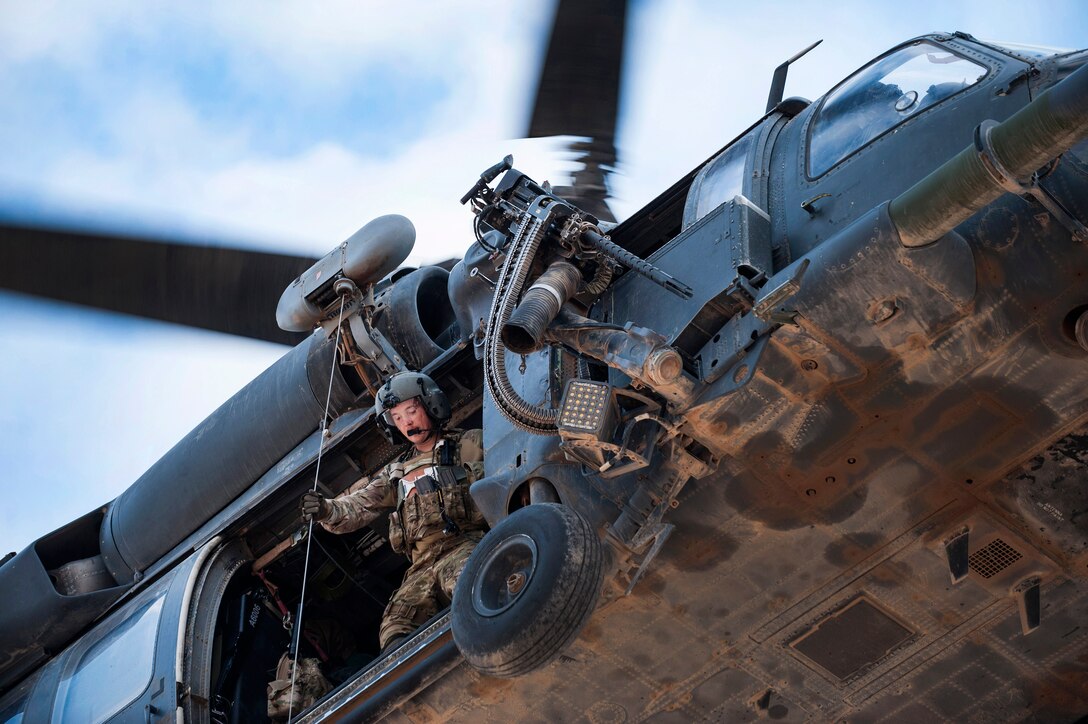 An airman stands at the open door of a helicopter in flight.