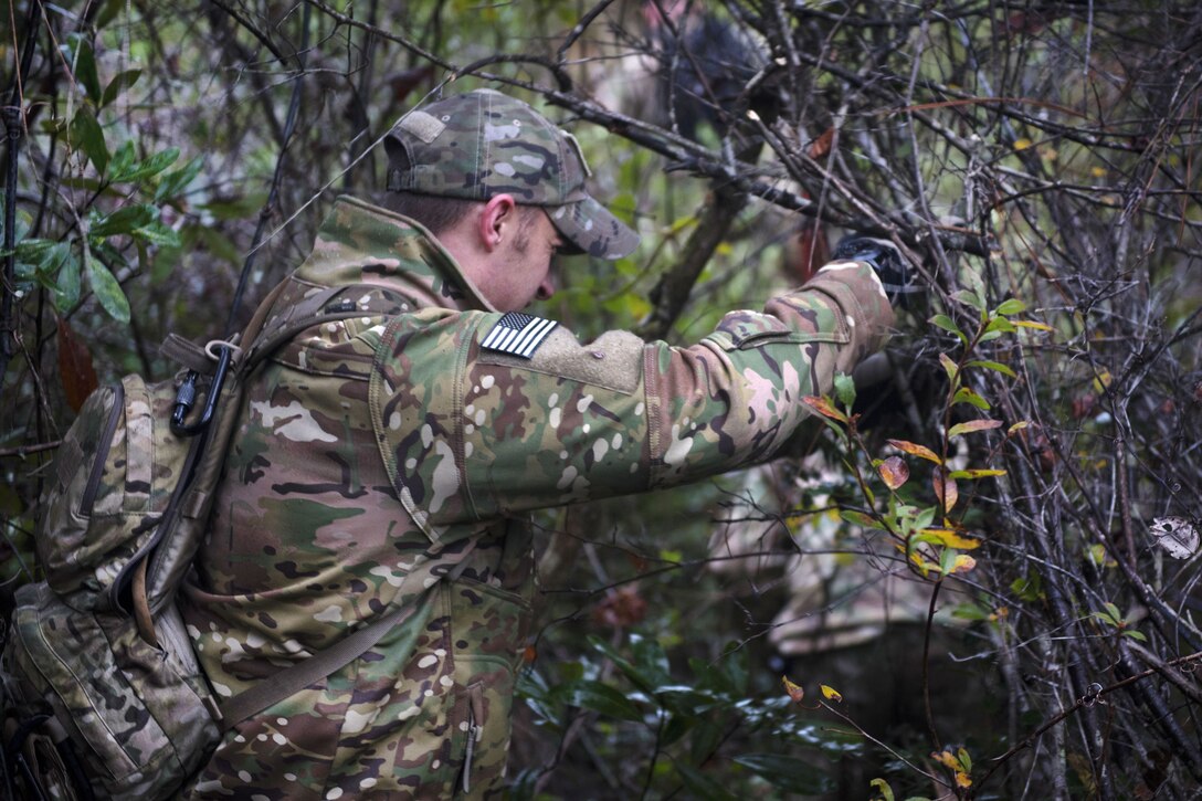 An airman pushes his way through branches.