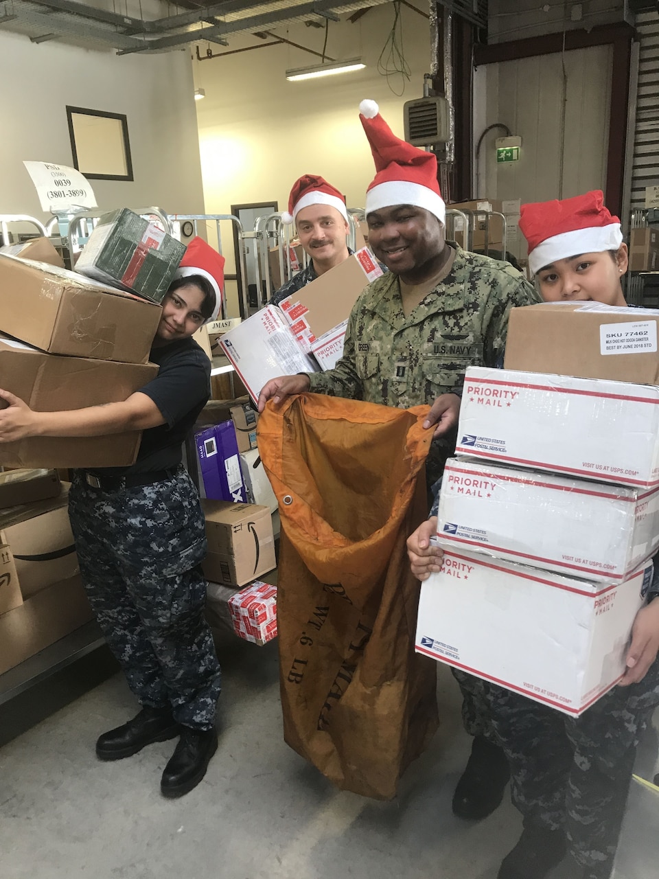 Navy Lt. Joseph Green, director of the fleet mail center in Sigonella, Italy, and sailors assigned to the center hold a small sample of the mail that flows through on its way to deployed units operating in the Mediterranean and tenant commands at Naval Air Station Sigonella.