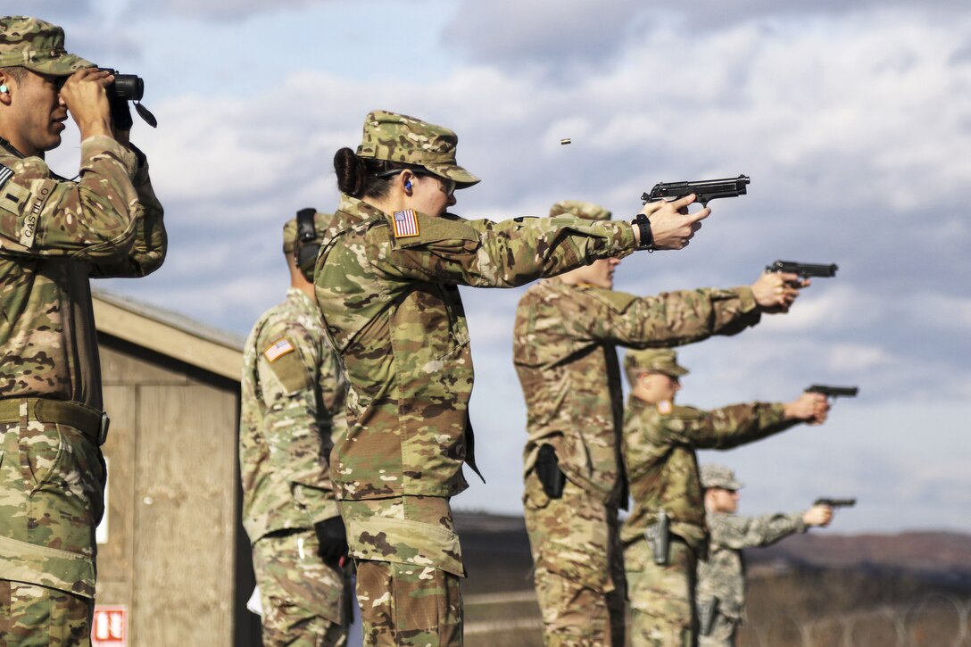 Soldiers standing in a line fire pistols.