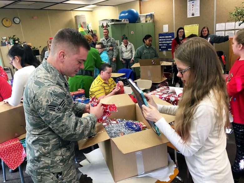Senior Airman Jordan Given, 67th Aerial Port Squadron, helps Avonlea unpack a box of gifts during a Christmas party