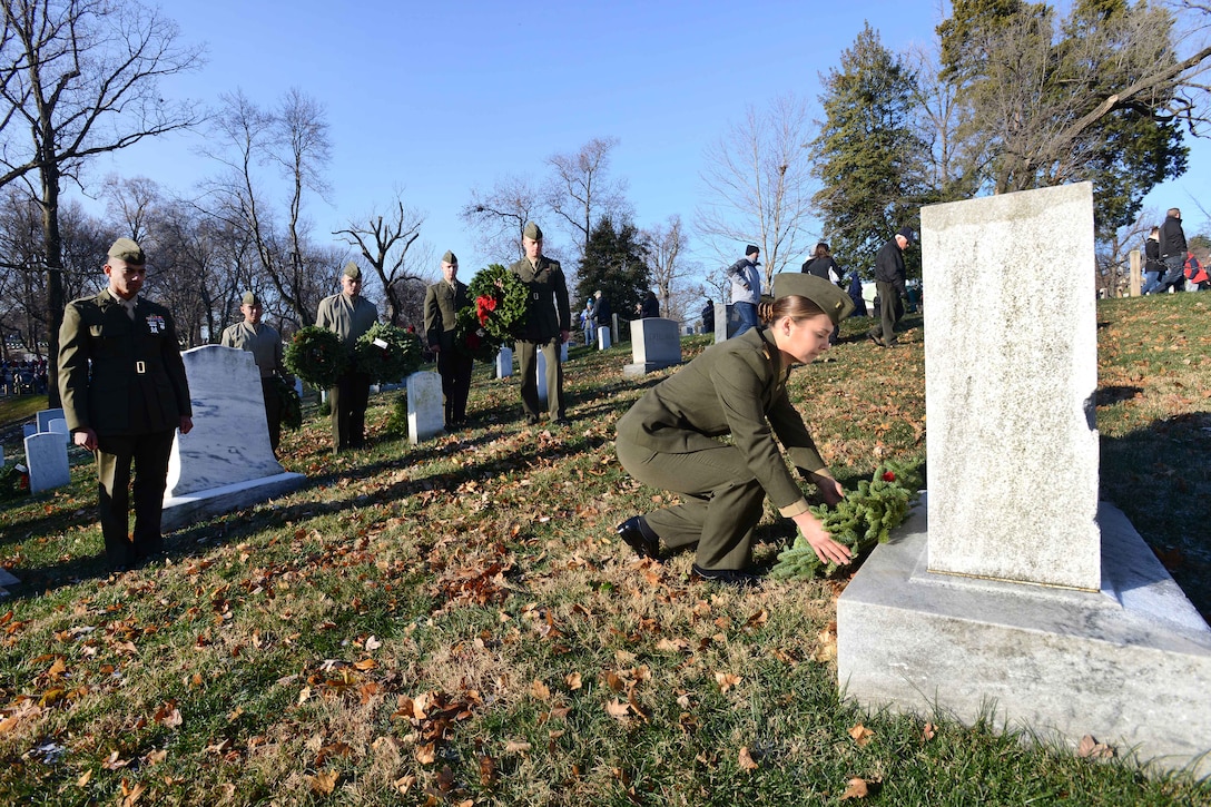 A Marine kneels to place a wreath on a gravestone.