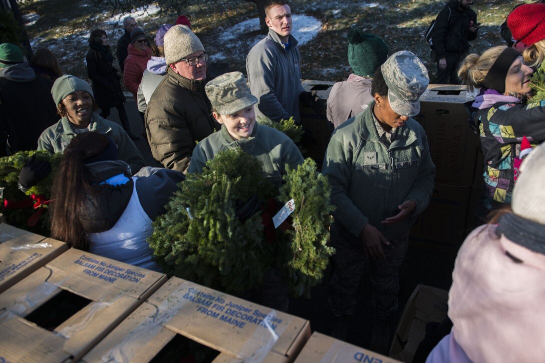 Three airmen pass out wreaths to people.