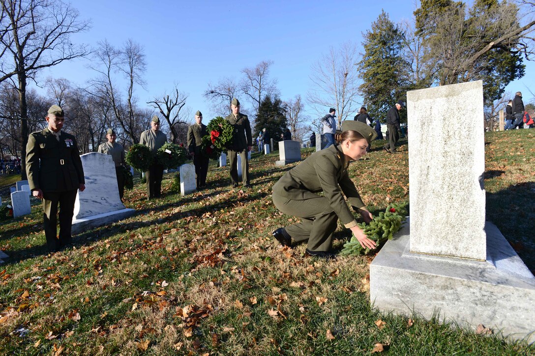 A Marine kneels to place a wreath on a gravestone.