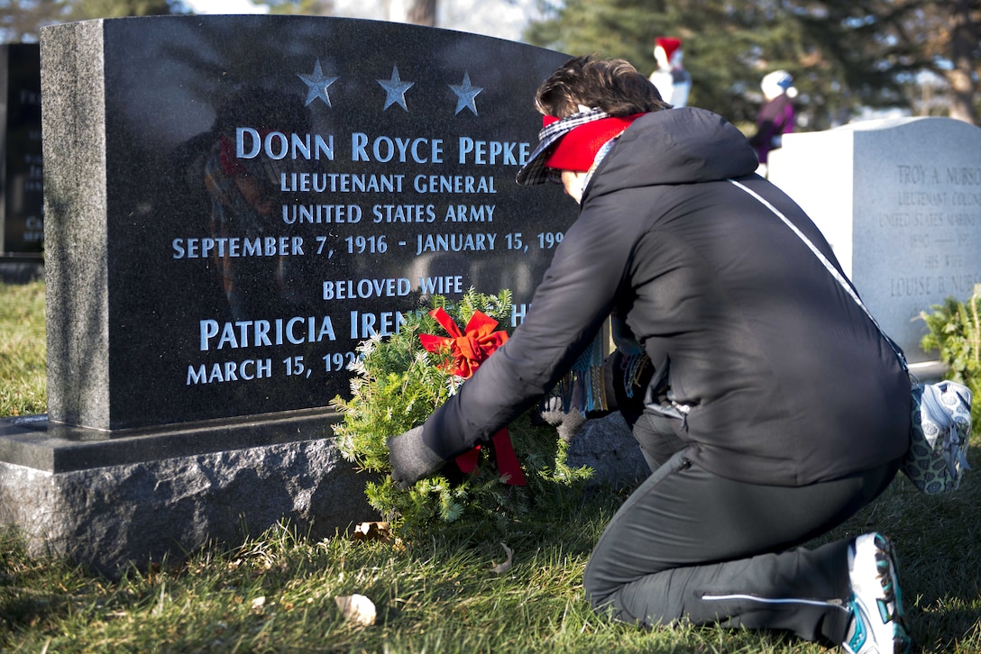A person kneels to place a wreath at a headstone.