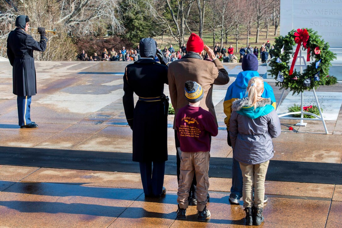 A soldier and civilians saute and place their hands over their hearts in front of a tomb.