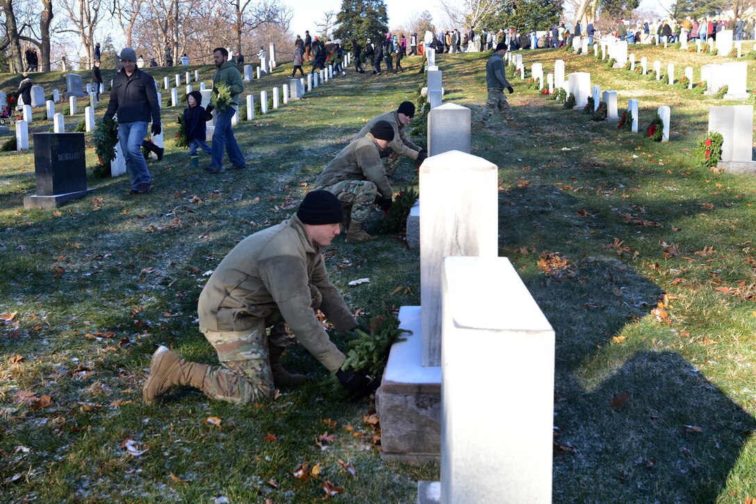Army Sgt. Nathan Lynnes, foreground, Sgt. Adam Lynnes, center, and Staff Sergeant Tyler Wuff place wreaths on grave markers.