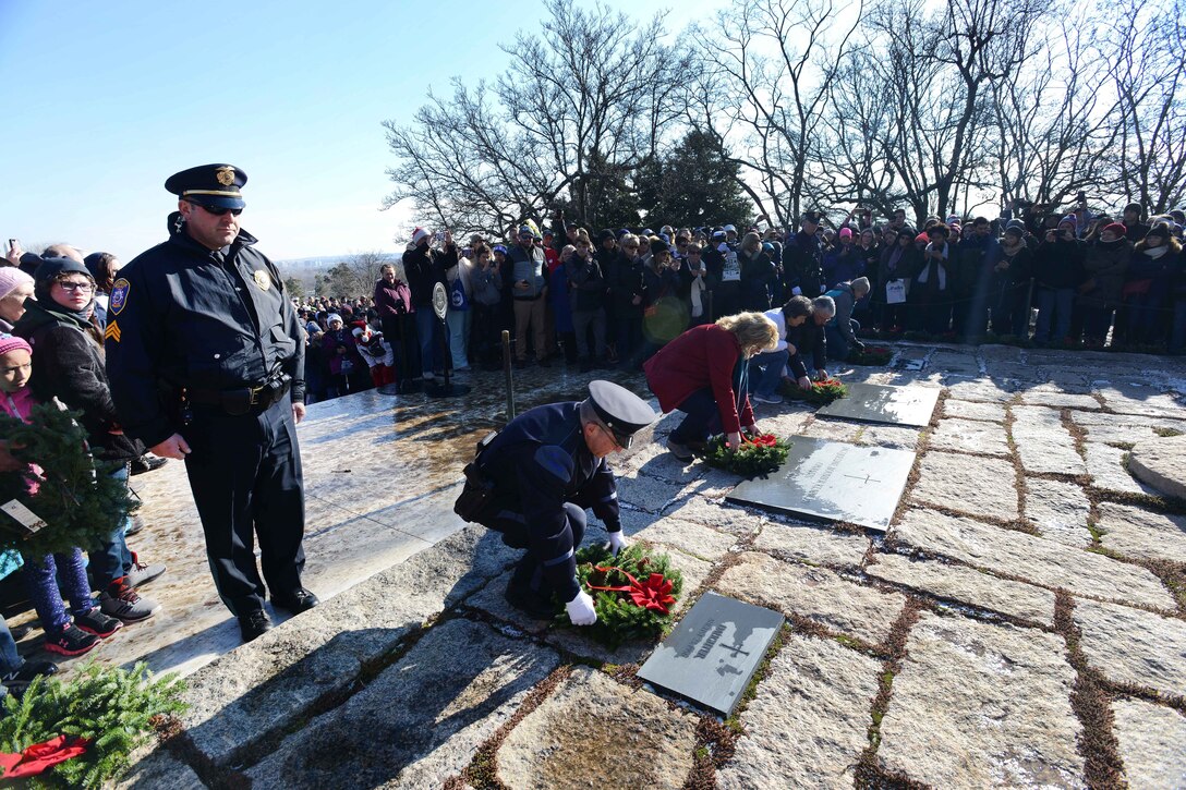 People kneel to place wreaths at grave markers.