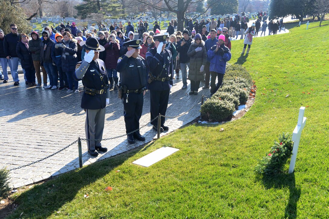 A line of police officers salute with a crowd behind them.