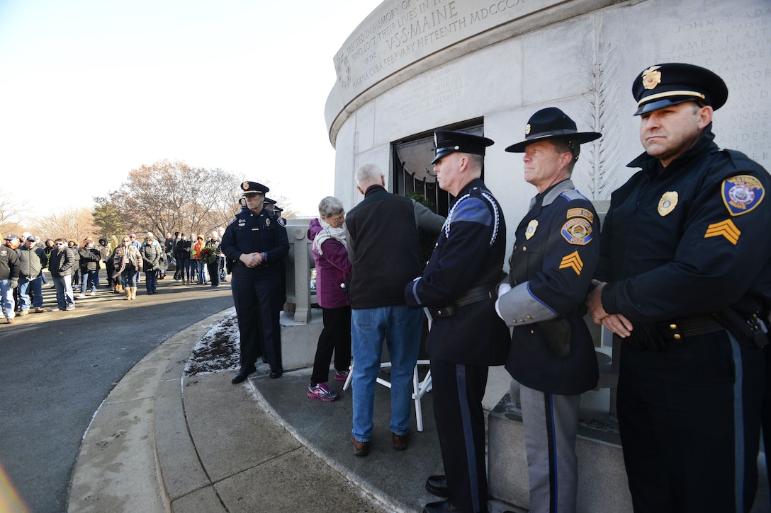 A row of police officers stand while two people place a wreath.