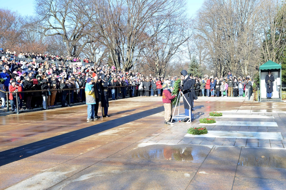 A soldier and civilians place a wreath at a tomb.