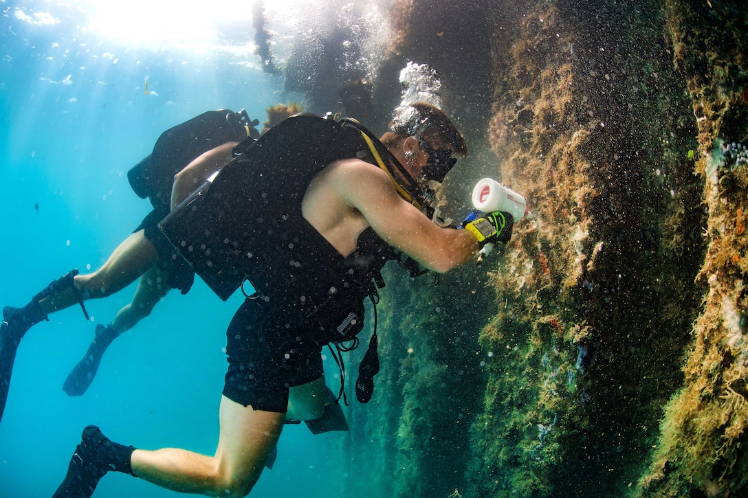 A Navy diver conducts an underwater pier survey using ultra sonic testing tools.