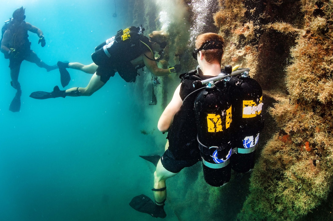 Navy divers conduct an underwater pier survey.