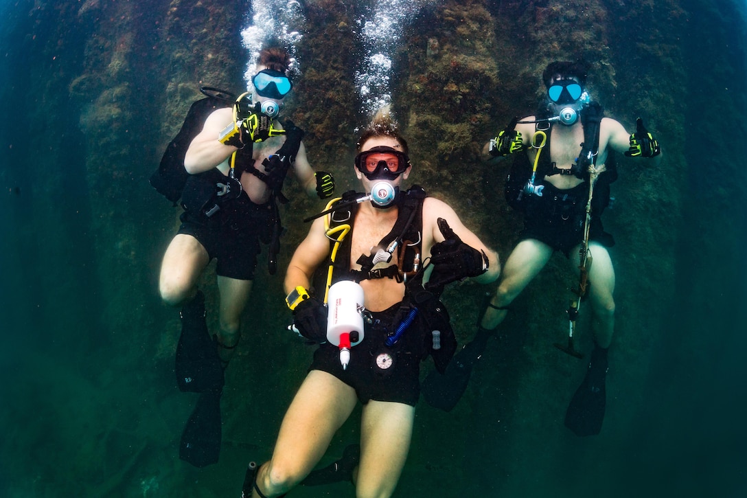 Three Navy divers pose for an underwater photograph.