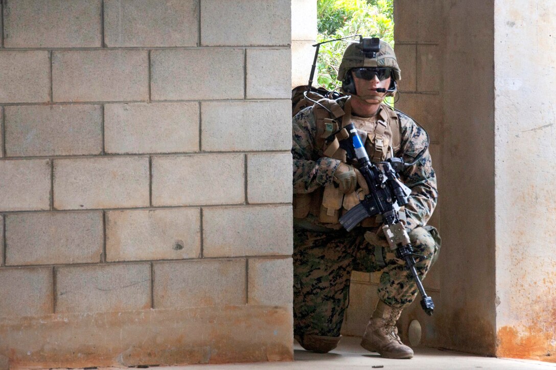 A Marine kneels while holding a gun.