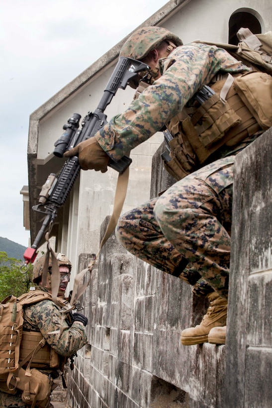 A Marine with a gun climbs over a wall.
