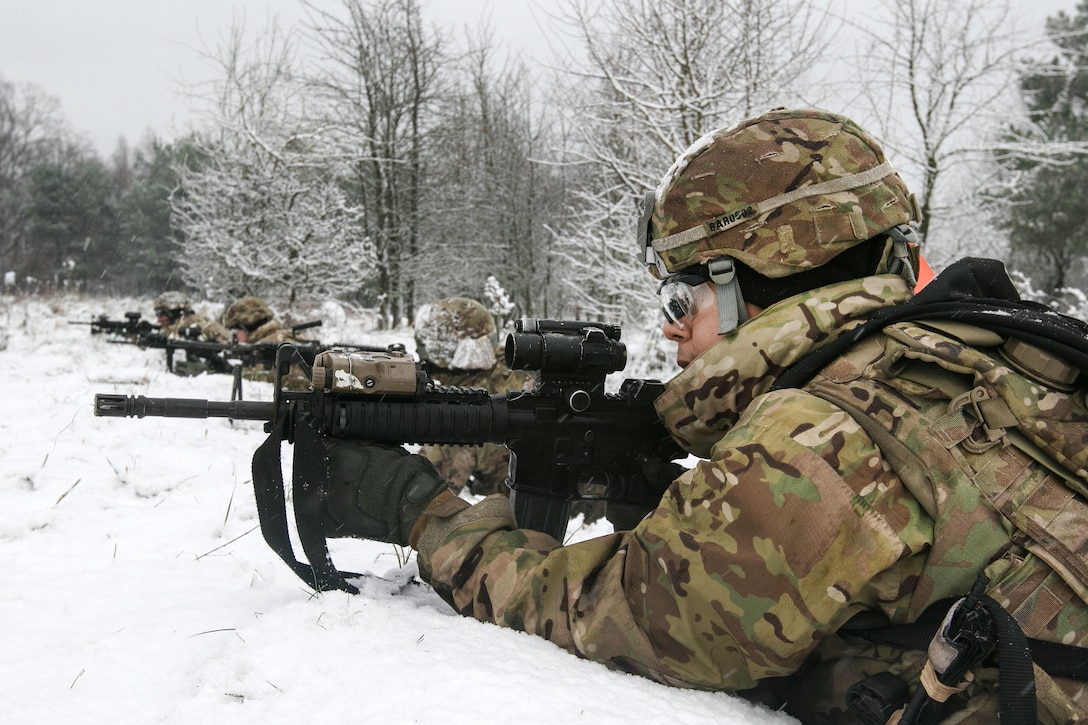 Soldiers aim firearms from behind a snow covered berm.