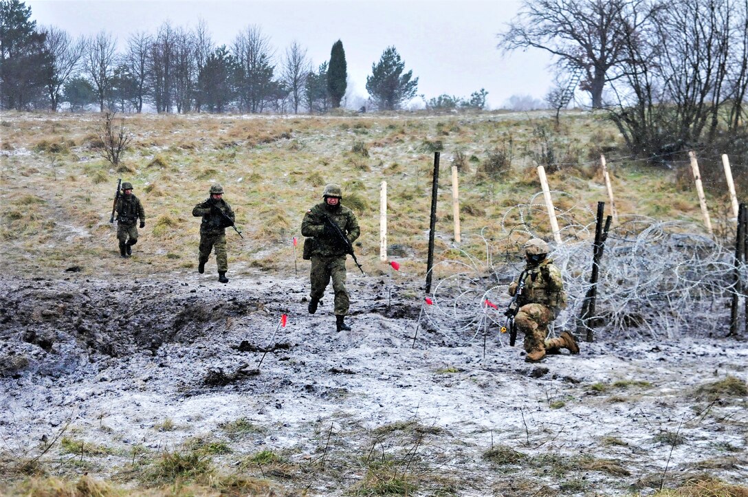 A U.S. soldier kneels and points while Polish soldiers run.