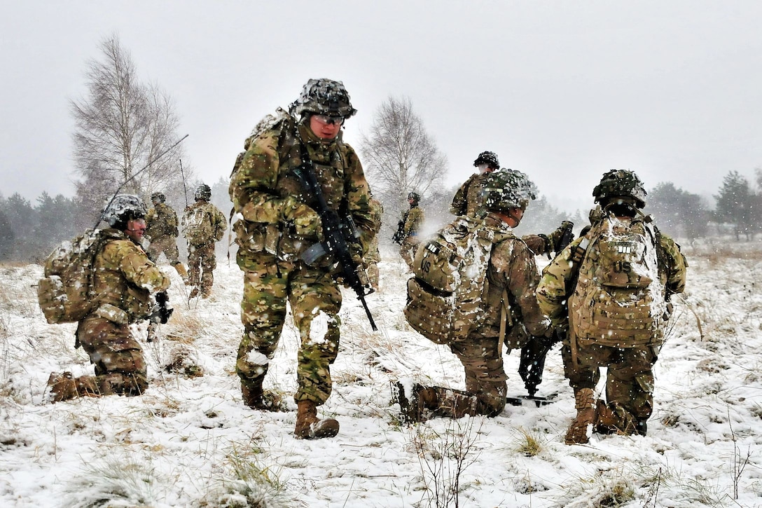 Soldiers kneel and move around a field with snow.