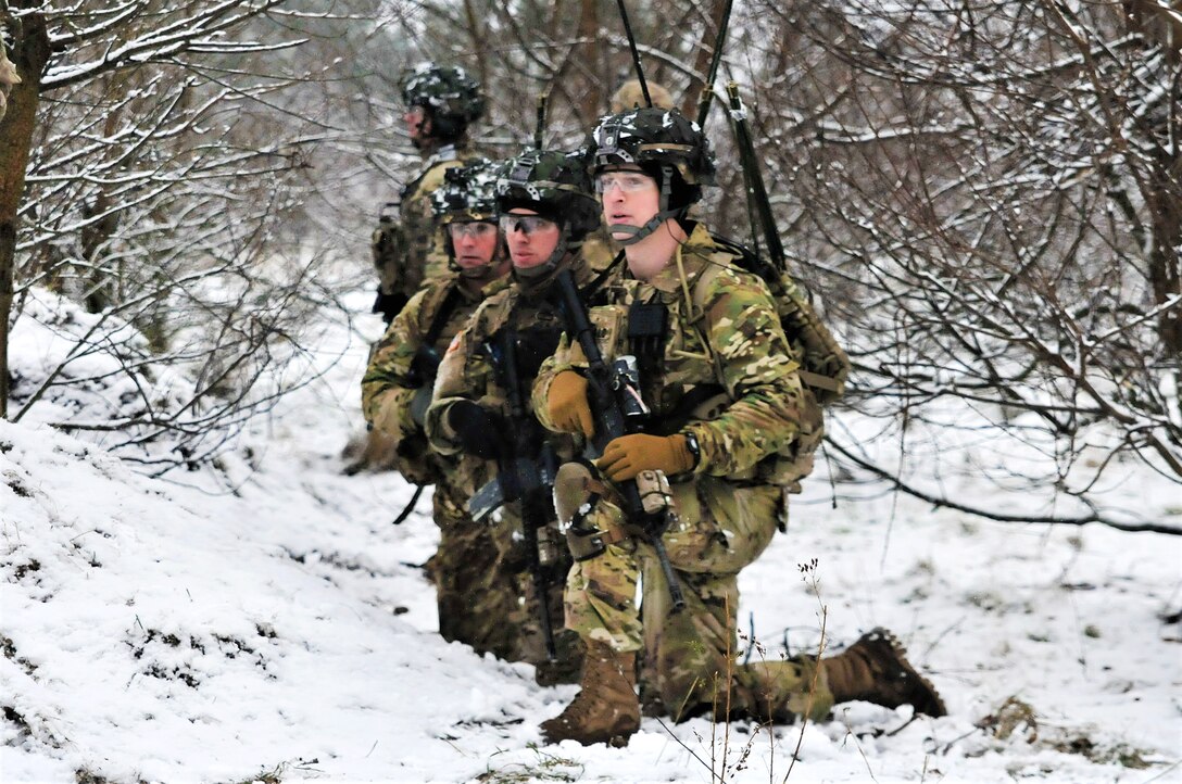 A row of soldiers kneel and look off camera.