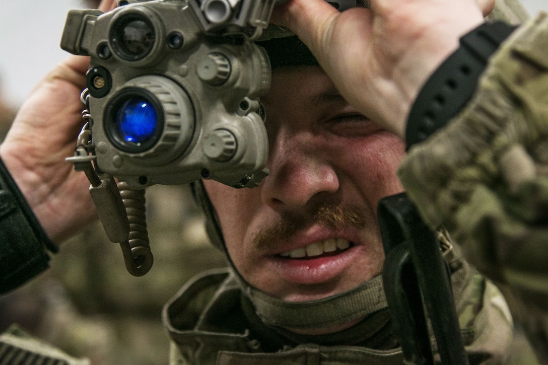 A soldier adjusts equipment near his face.