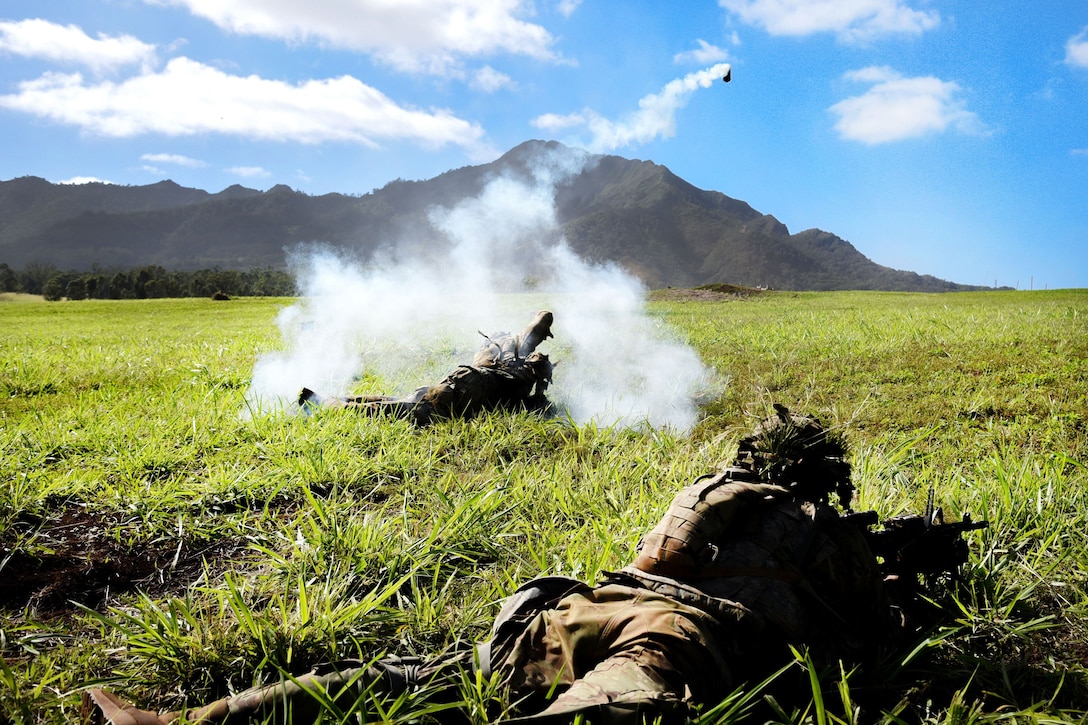 A soldier laying on the ground throws a smoke flare.