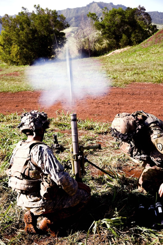 Soldiers kneel on the ground and fire a mortar.