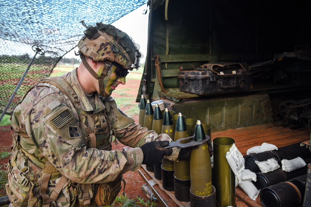 A soldier uses a tool on rounds sitting on the back of the truck.