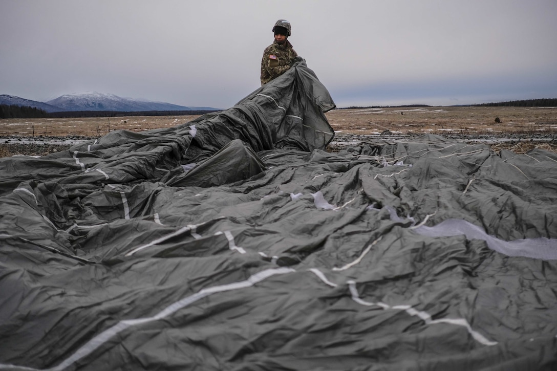 A paratrooper gathers a parachute after training.