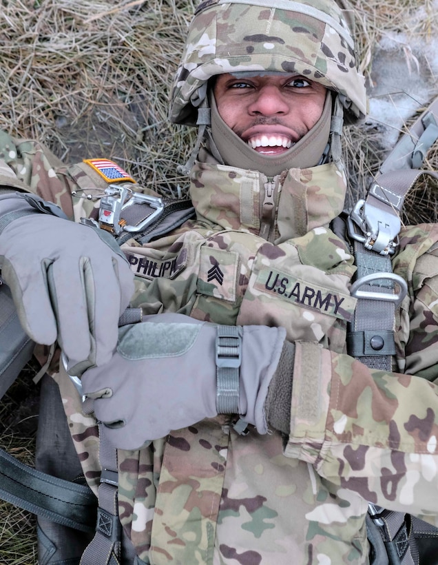 A soldier smiles while lying in grass.