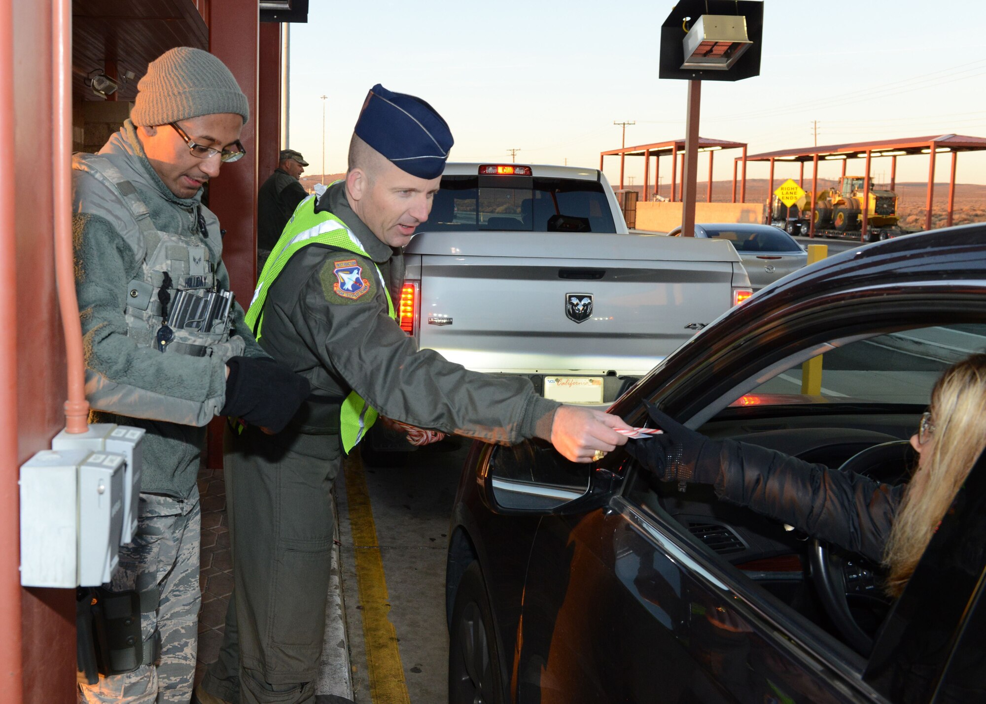 Col. Matthew Higer, U.S. Air Force Test Pilot School commandant, hands a candy cane and holiday card to a motorist at Edwards AFB’s North Gate Dec. 18. The colonel teamed up with Airman 1st Class Jerome Holliday, 412th Security Forces Squadron, for the morning. (U.S. Air Force photo by Kenji Thuloweit)