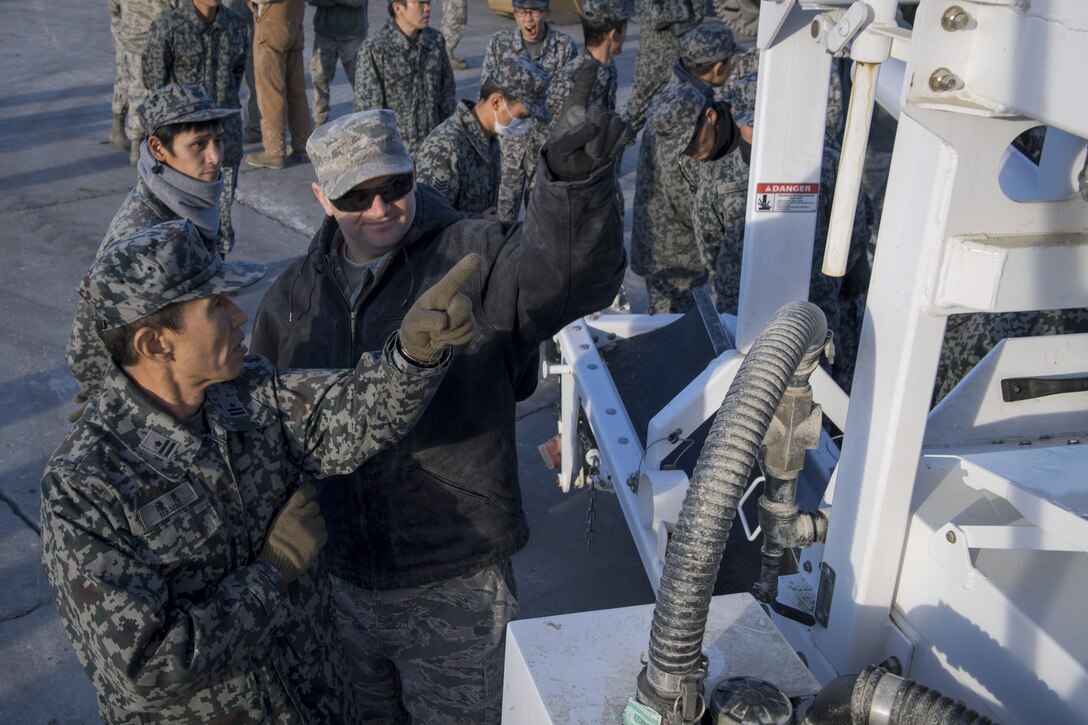 A U.S. Air Force Airman with the 374th Civil Engineer Squadron points out equipment components to a Koku Jietai (Japan Air Self-Defense Force) engineer during a rapid airfield damage repair demonstration, Dec. 12, 2017, at Yokota Air Base, Japan.