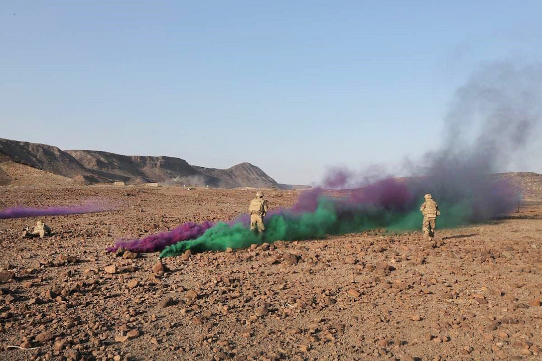Soldiers stand in colored smoke.
