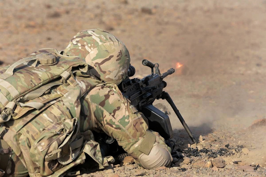 A soldier lays on the ground and fires a weapon.