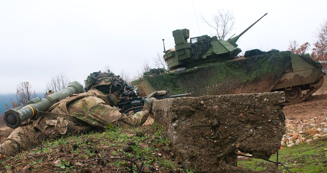 A soldier provides security after dismounting a M2 Bradley fighting vehicle during live-fire.