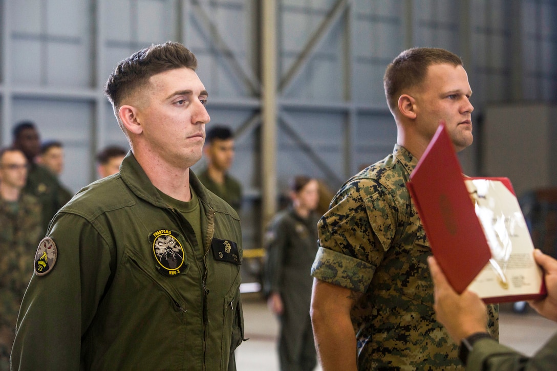 Sgt. Ethan Mintus and Sgt. Joseph Latsch, both unmanned aerial system operators with Marine Unmanned Aerial Vehicle Squadron 3, wait to be awarded during a ceremony at Hangar 103, Marine Corps Air Station Kaneohe Bay, Dec. 11, 2017. They were awarded the Navy and Marine Corps Achievement Medal with the newly authorized Remote Impact “R” Device for their performance during combat operations.