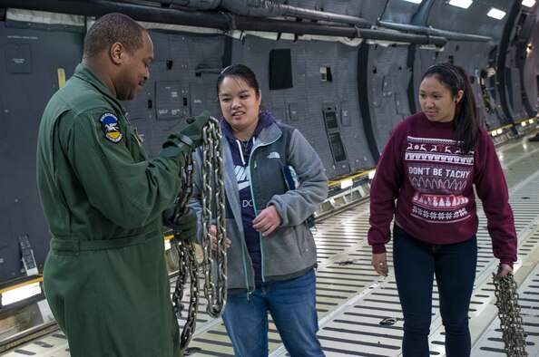 Master Sgt. Bryan Boyd, 356th Airlift Squadron load master, shows Kelly Kamiya and Karizza Cruz the different chains that are used to tie down cargo during a walk-through tour of a C-5M Super Galaxy aircraft December 18, 2017 at Joint Base San Antonio-Lackland, Texas.