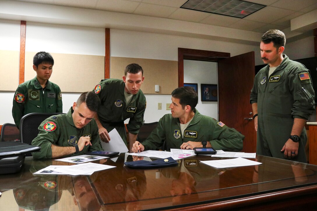 U.S. and Japanese airmen sit at a table and look over paperwork.