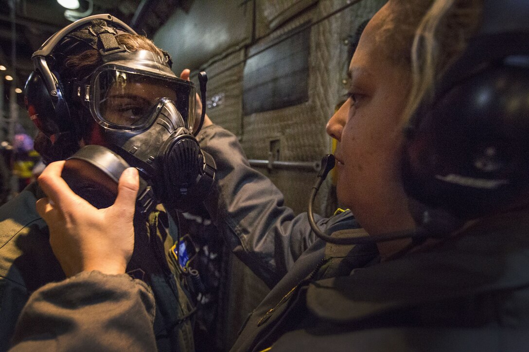An airman checks the gas mask worn by another airman.