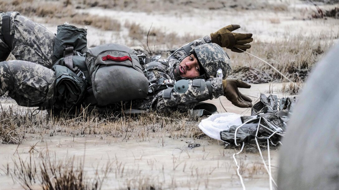 A soldier lies on the ground and reaches his arms above his head.