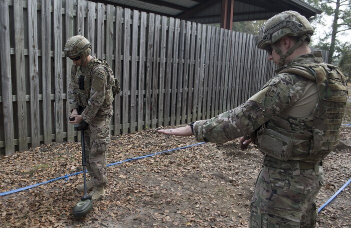 1st Lt. Paul Underwood, searches for mines SrA Koser, Matthew Civil Engineer Squadron Explosive Ordnance Disposal technician searches for mines while Senior Airman Matthew Koser, 628th CES EOD technician instructs him on proper techniques during the EOD Olympics Dec. 15, 2017.